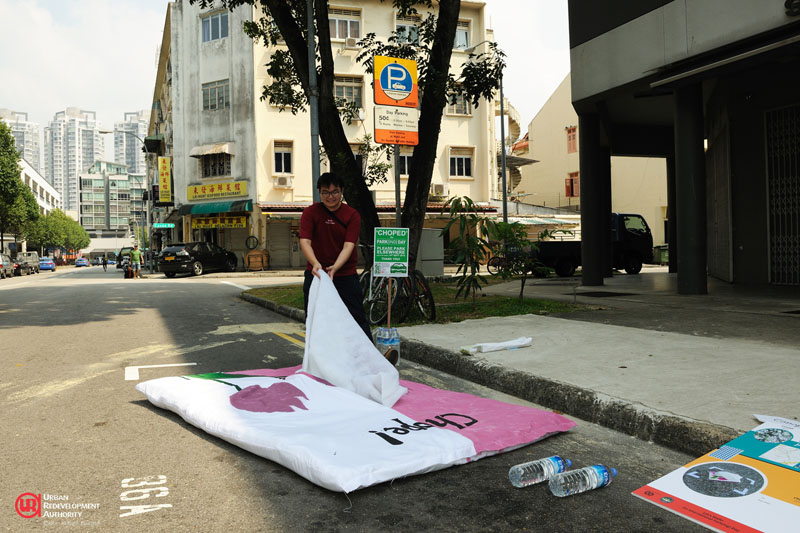 A SUTD student brings a uniquely Singaporean tradition to the road – reserving a space with a tissue packet during PARK(ing) Day 2014. | URA